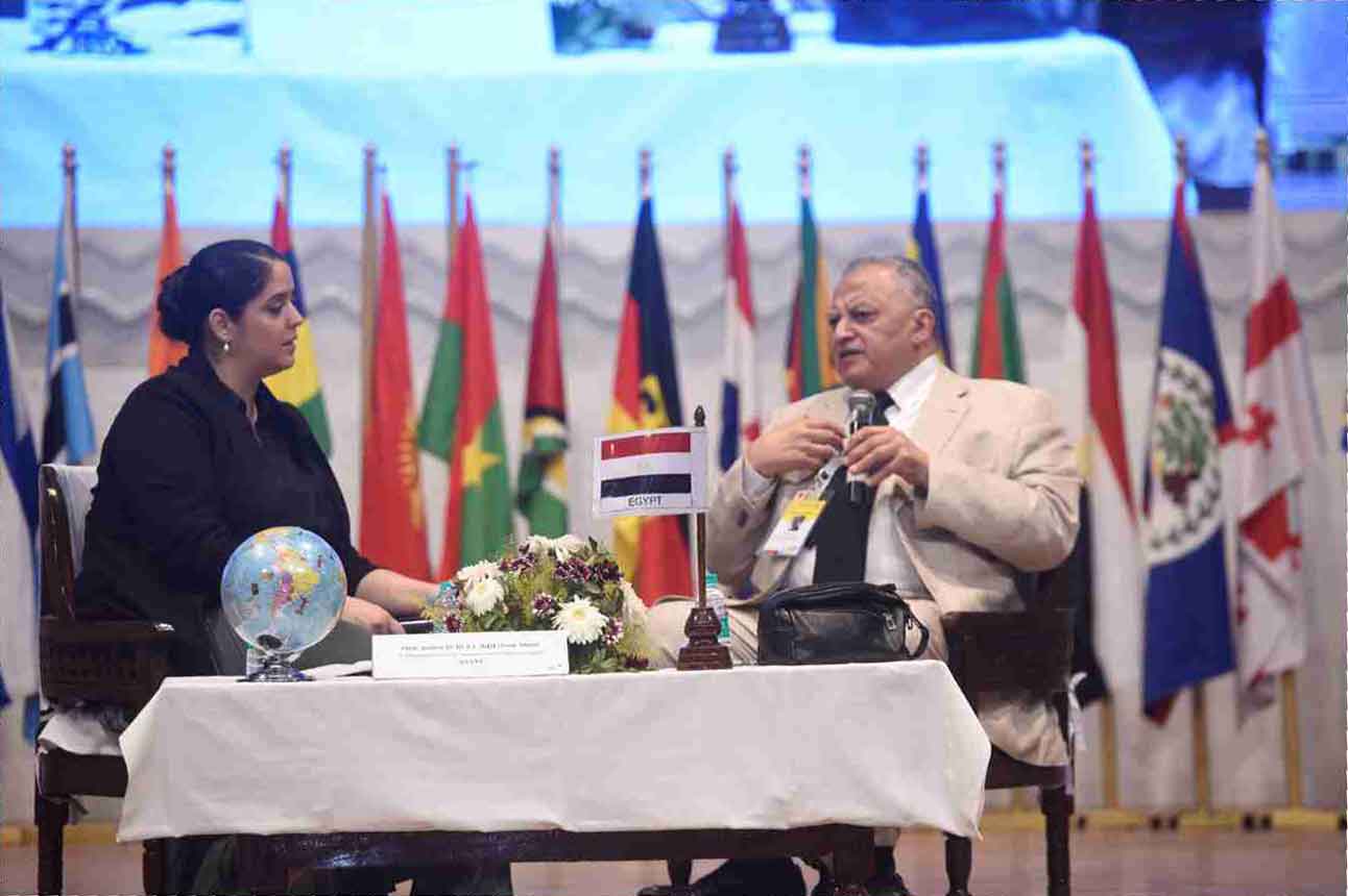 A panel discussion on stage in front of a row of national flags from many countries